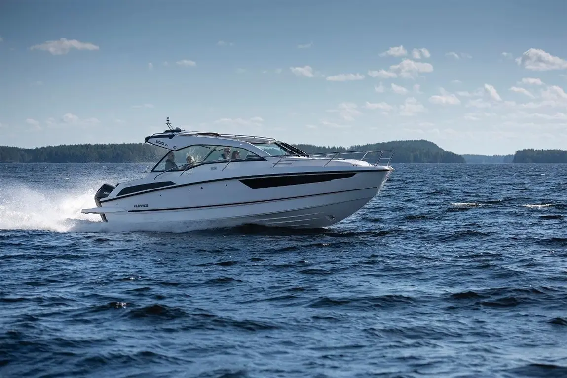 A modern white motorboat named "Flipper" speeds across blue water, with green forests in the background and a clear sky.